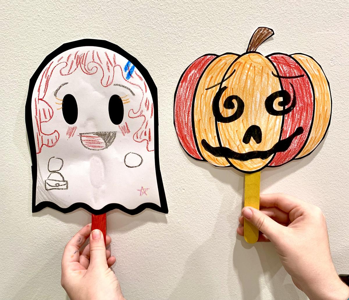 Cute paper puppets on popsicle sticks. On the left is a smiling ghost and on the right is a smiling pumpkin